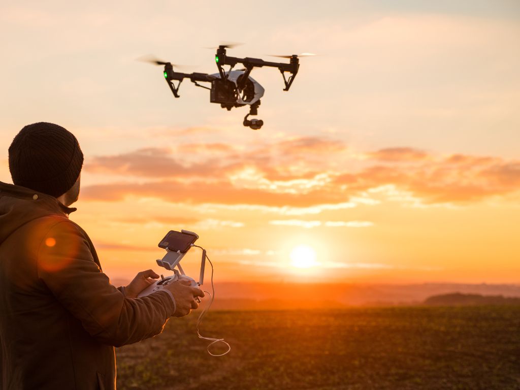 Man operating a drone with a sunset in the background